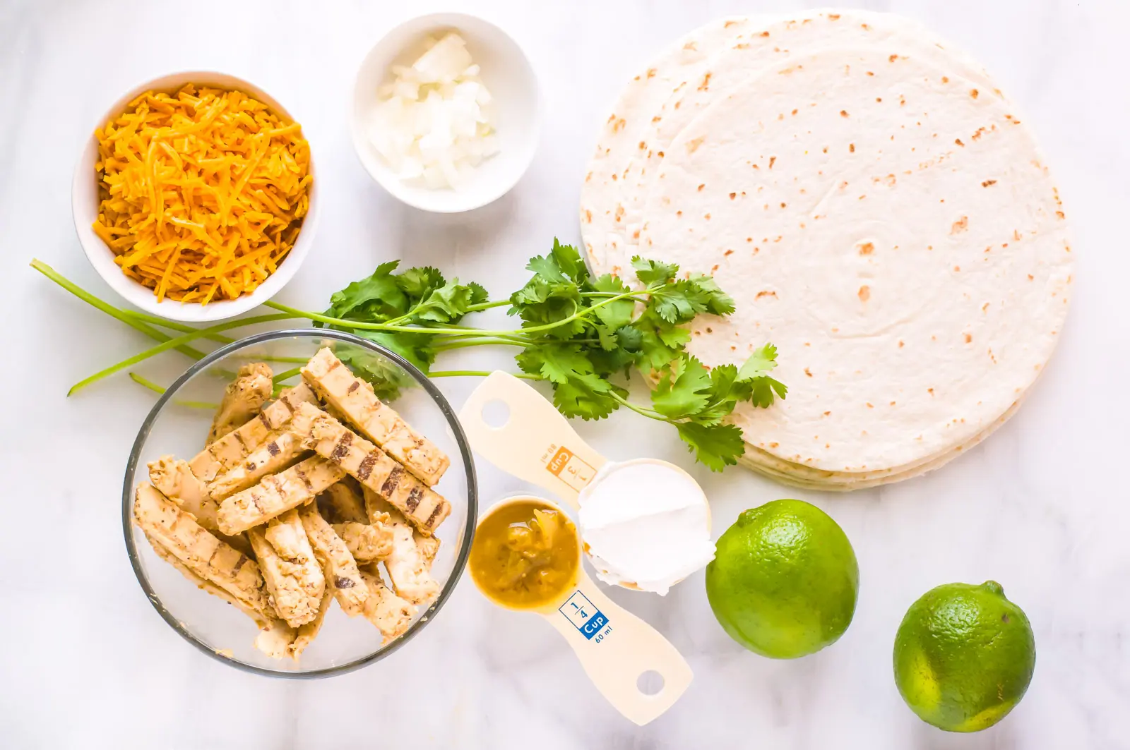 Looking down on ingredients such as flour tortillas, limes, fresh cilantro, chopped onion, and more.
