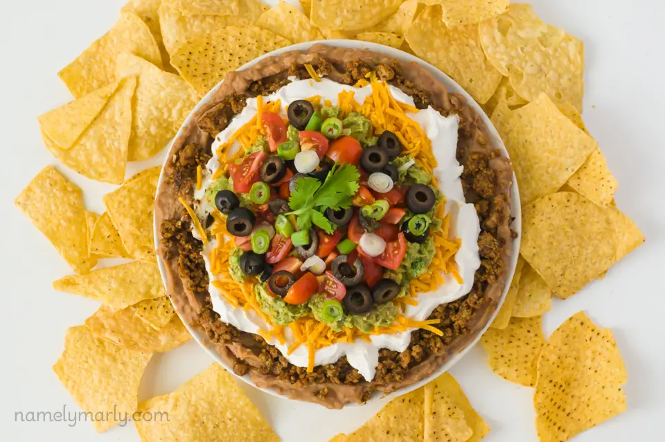 Looking down on a plate full of vegan 7 layer dip surrounded by tortilla chips.
