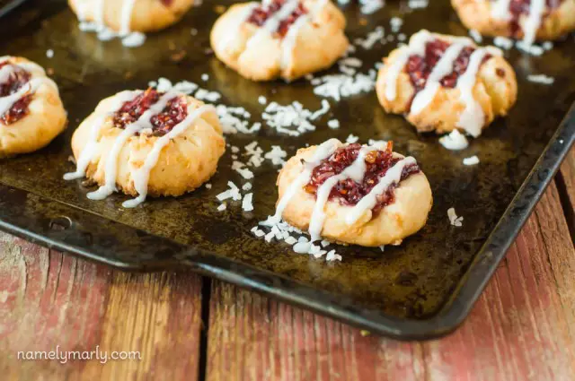 Several Raspberry Coconut Thumbprint Cookies in a row on a baking sheet.