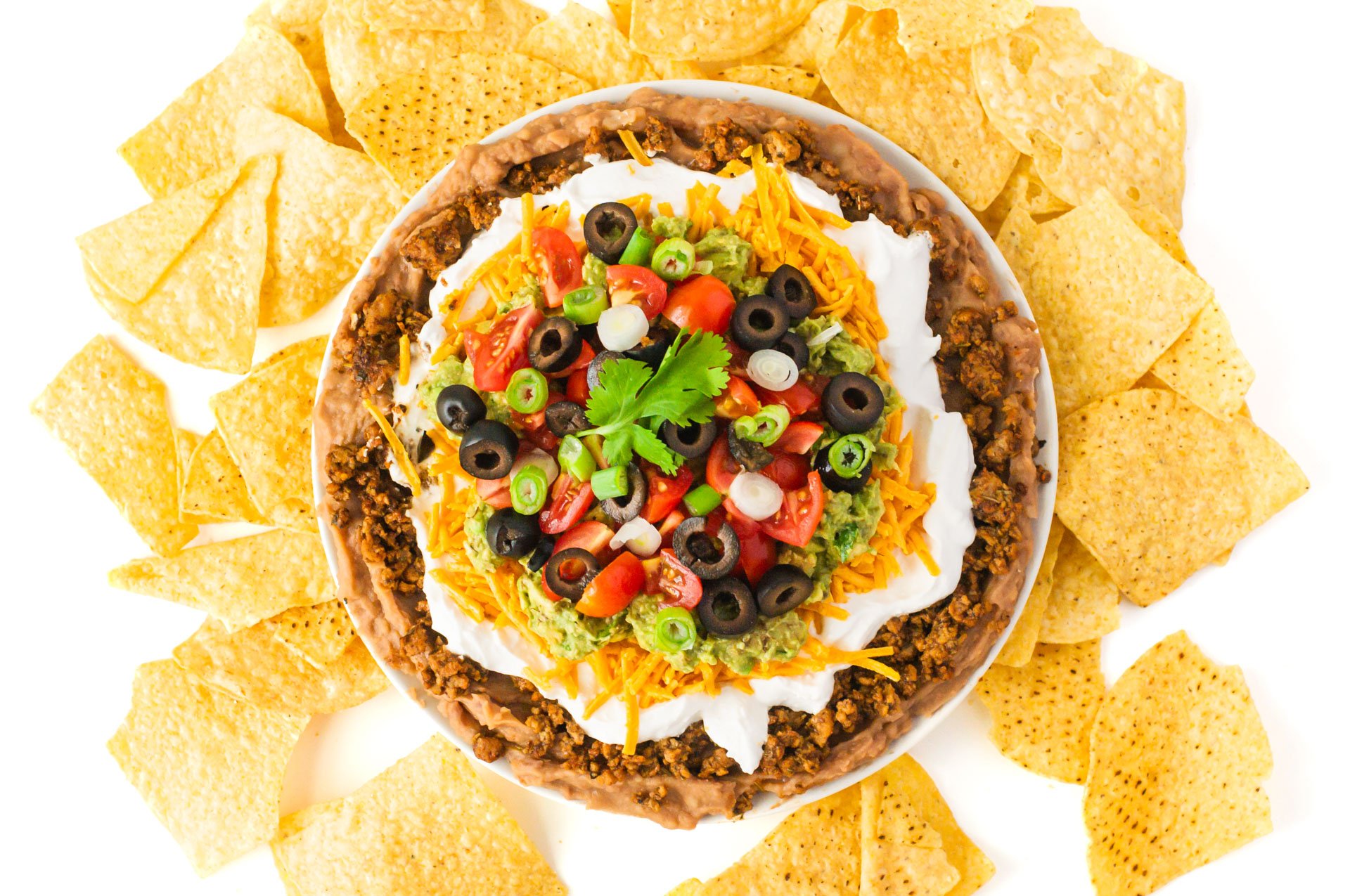 Looking down on a plate full of vegan 7 layer dip surrounded by tortilla chips.