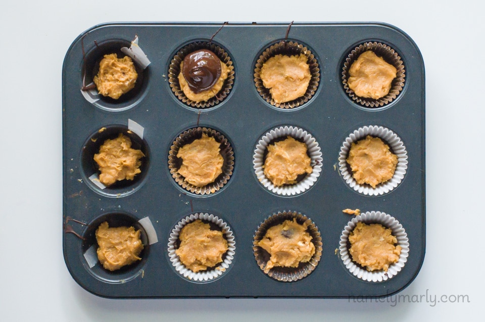 A tray of a mini muffin pan holds chocolate candies being made into peanut butter cups.