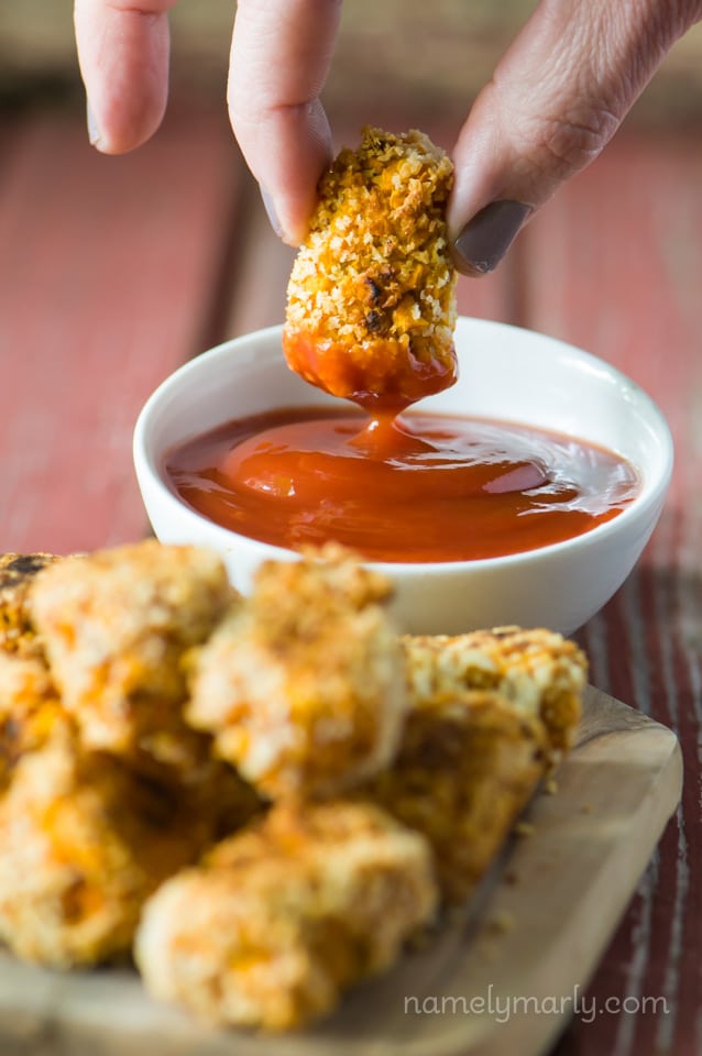 A hand holds a tater tot and is dipping it in the bowl of ketchup.