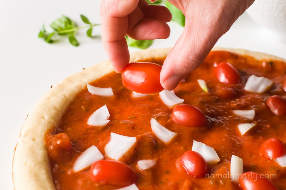 A hand holds a cherry tomato and is placing it on a pizza.