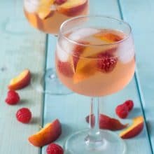 Two wine glasses with peach sangria with fresh raspberries and fresh peach slices.