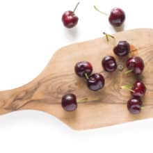 Several fresh cherries on a wooden cutting board.