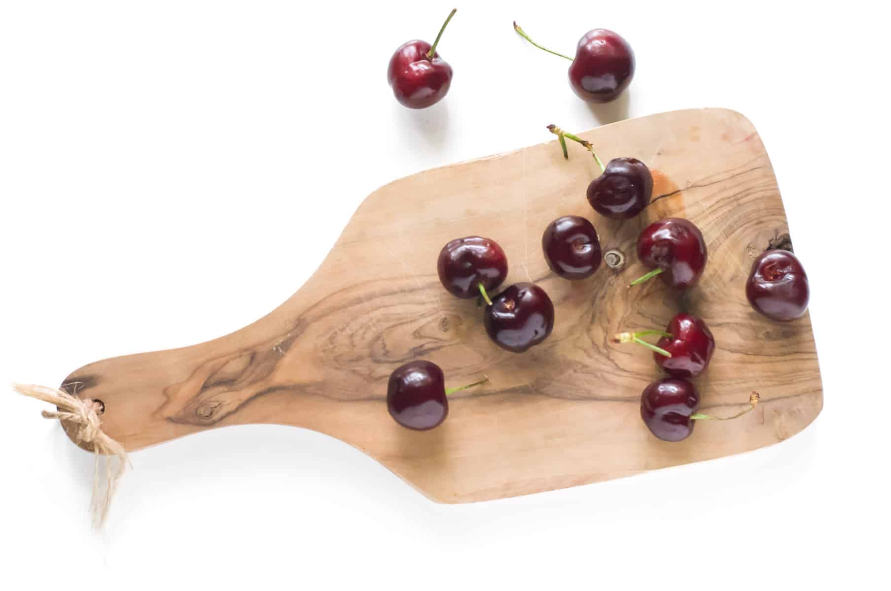 Several fresh cherries on a wooden cutting board.