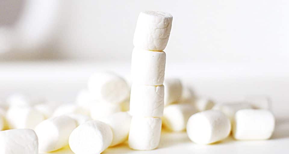 A stack of 4 marshmallows has more marshmallows scattered around beside it.