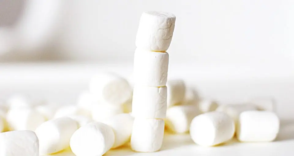 A stack of 4 marshmallows has more marshmallows scattered around beside it.