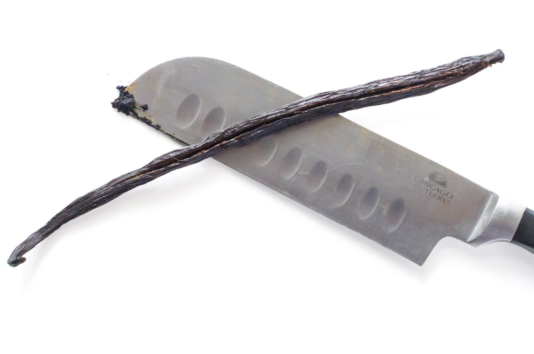 A vanilla bean pod sits on top of a knife with vanilla scrapings on it.