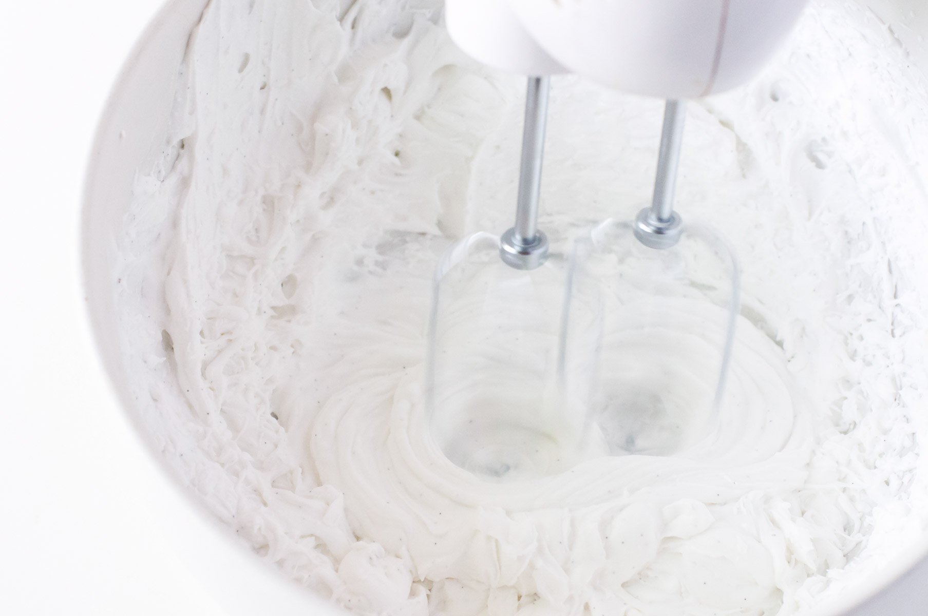 A hand-held mixer is whipping up the chilled coconut fat.