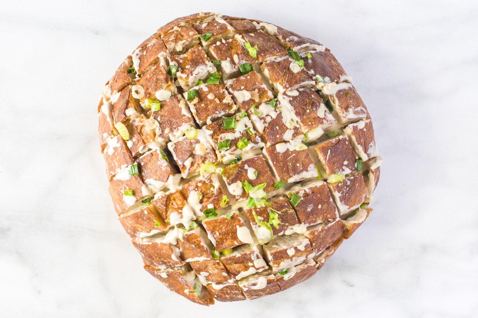 A round loaf of bread sits on a cutting board. It has been cut into cubes with cheese and green onions on top.