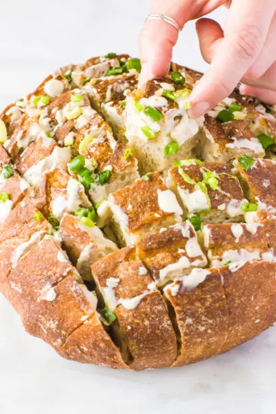 A hand pulls out a piece of cheesy vegan pull-apart bread.