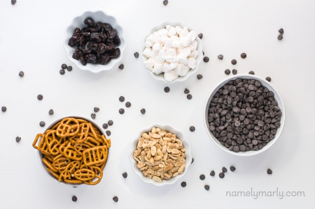 Looking down on ingredients in bowls, like pretzels, nuts, chocolate chips, marshmallows and dried fruit.