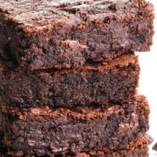 A stack of four brownies shows melted chocolate chips and there are more chocolate chips on the table beside them. The text on the image reads, Vegan Black Bean Brownies.