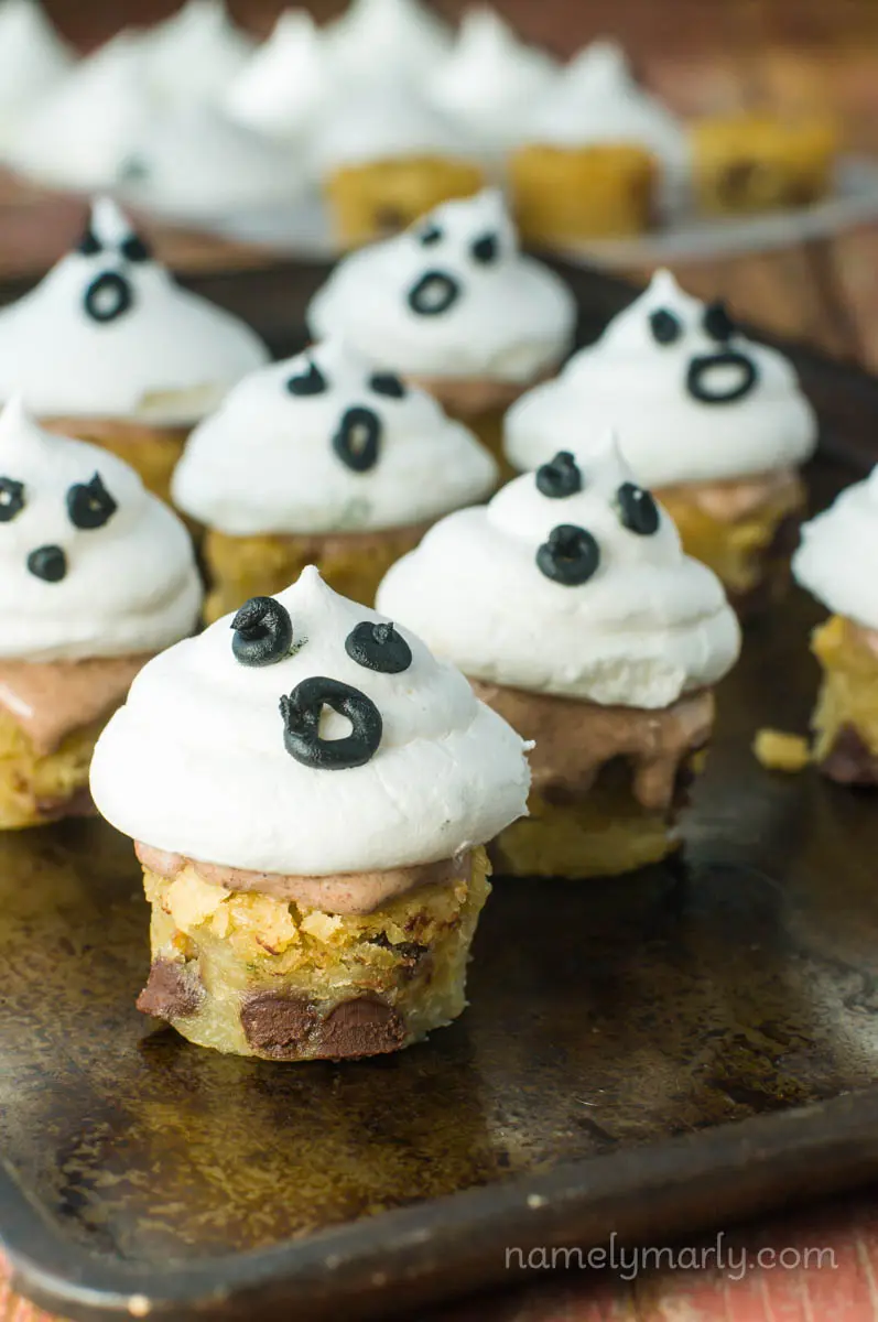 A baking sheet has several blondie bites topped with meringue puffs and black icing to look like a ghost face.