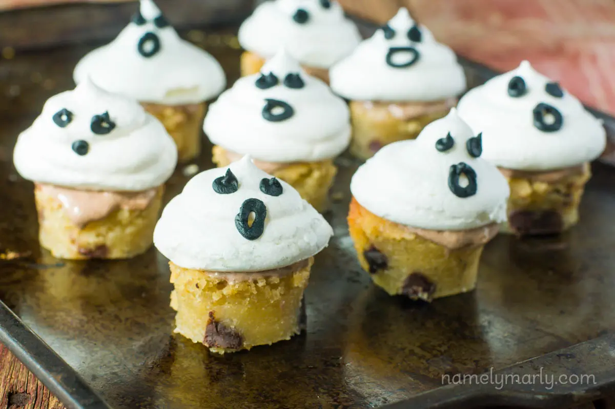 Several blondie bites are topped with vegan meringue puffs with black frosting to look like ghost faces.