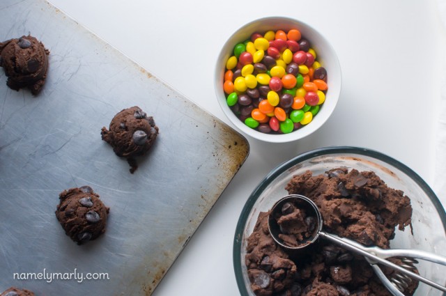 Looking down on a baking sheet with chocolate cookie dough balls and a bowl of skittles. 