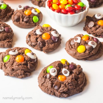 Several chocolate cookies have colorful candies and googly eyes on top.