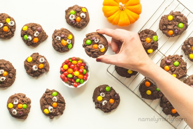 A hand reaches in to grab a Halloween monster cookie with googly eyes and skittles. 