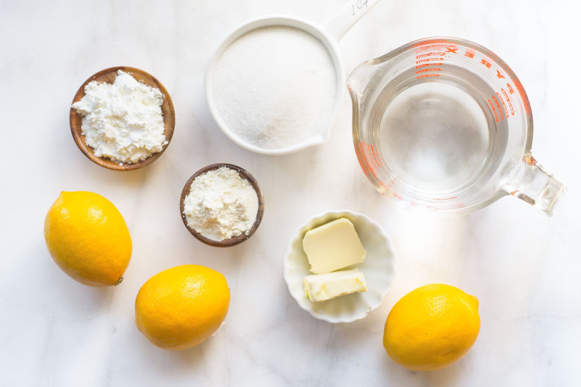 Looking down on ingredients on a counter, like sugar, water in a measuring cup, butter, lemons, etc.