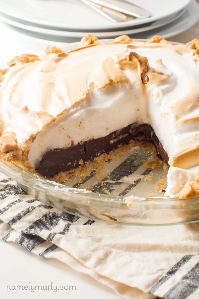 A pie has a slice cut out, showing chocolate pudding pie with a meringue on top.