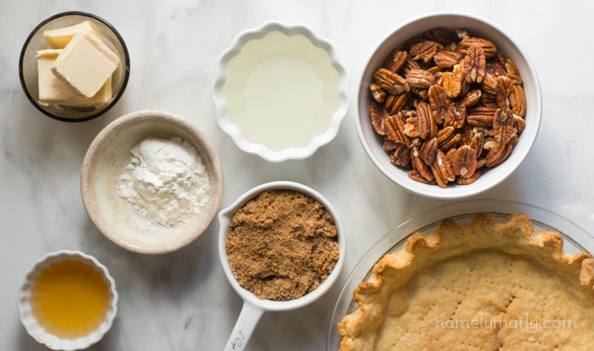 Ingredients for a pie sit on a white marble counter top, including vegan butter, pecans, and more.