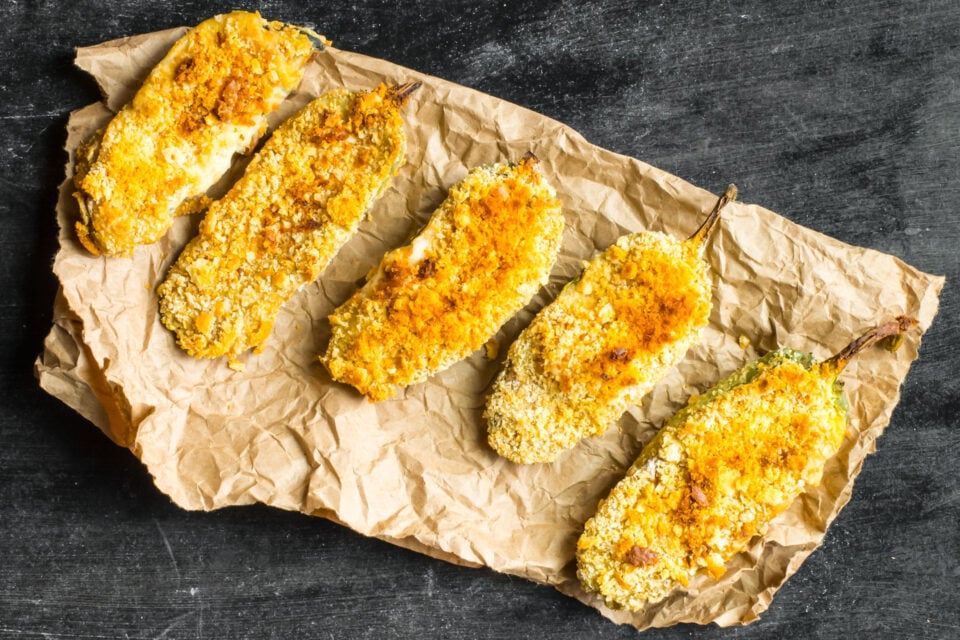 Looking down on several vegan baked jalapeño poppers on a piece of brown paper.