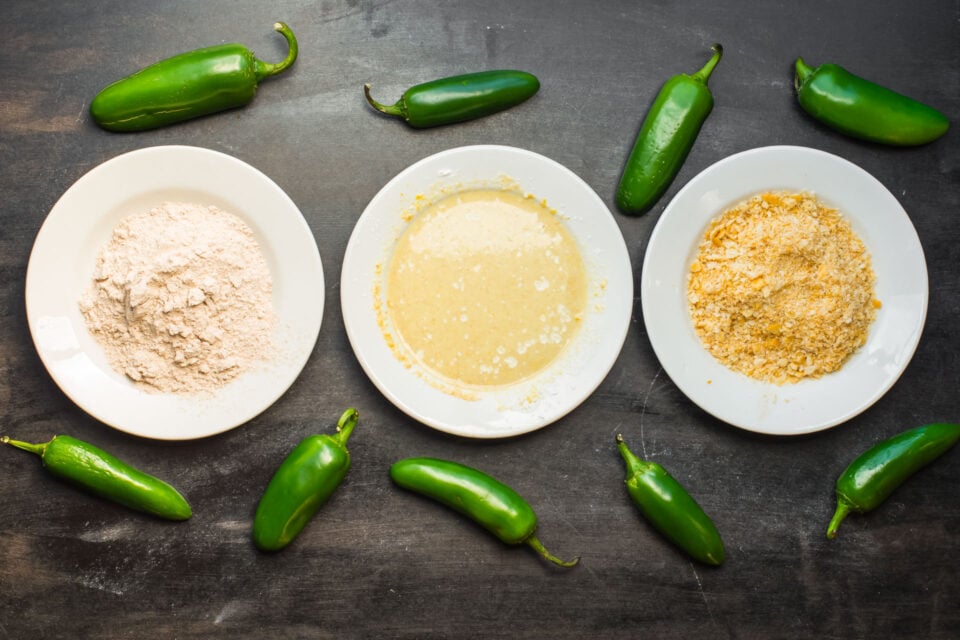 Three plates hold different dipping ingredients. There are several green jalapeños around the plates.