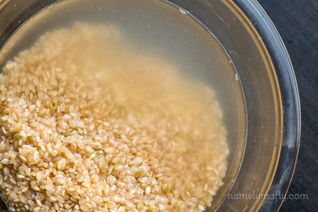 Looking down on rice in a bowl with water. The water is getting cloudy from the starches released from the rice.