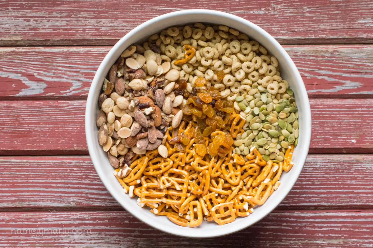 Looking down on a large bowl full of ingredients like cereal, pretzels, nuts, and more.