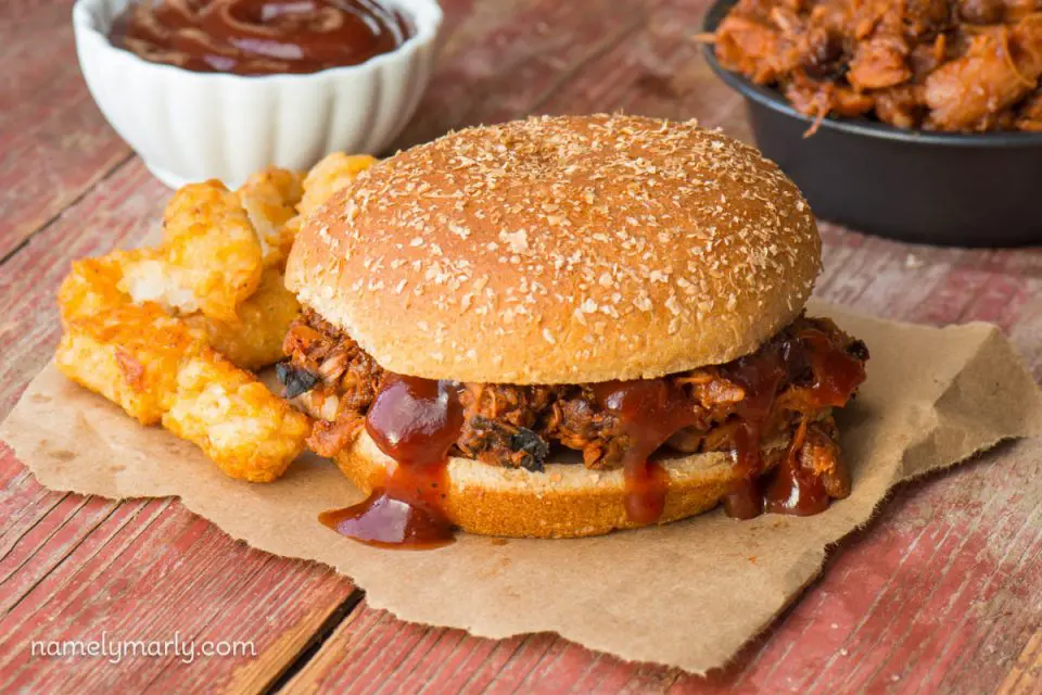 A vegan barbecue sandwich sits next to tater tots, sauce, and more "meat" filling.