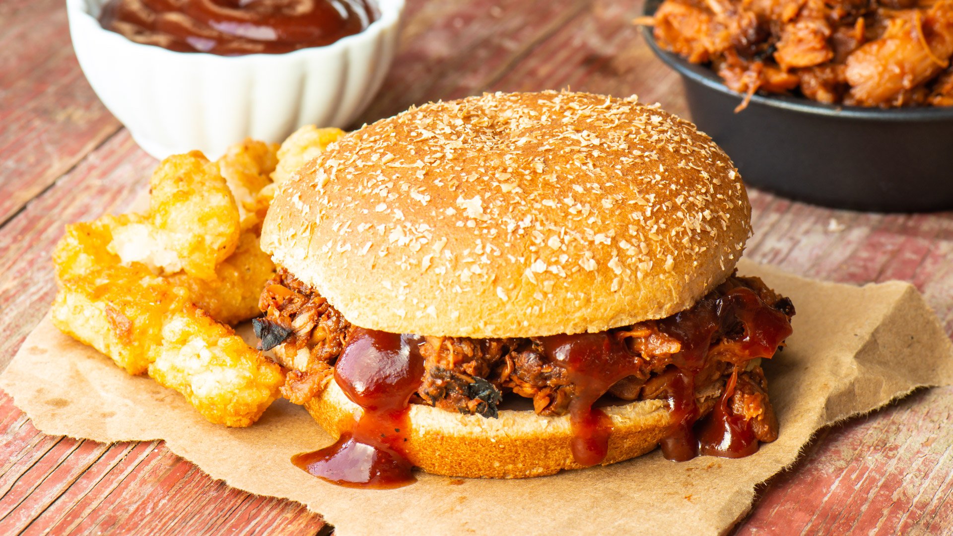 A vegan barbecue sandwich sits next to tater tots, sauce, and more "meat" filling.