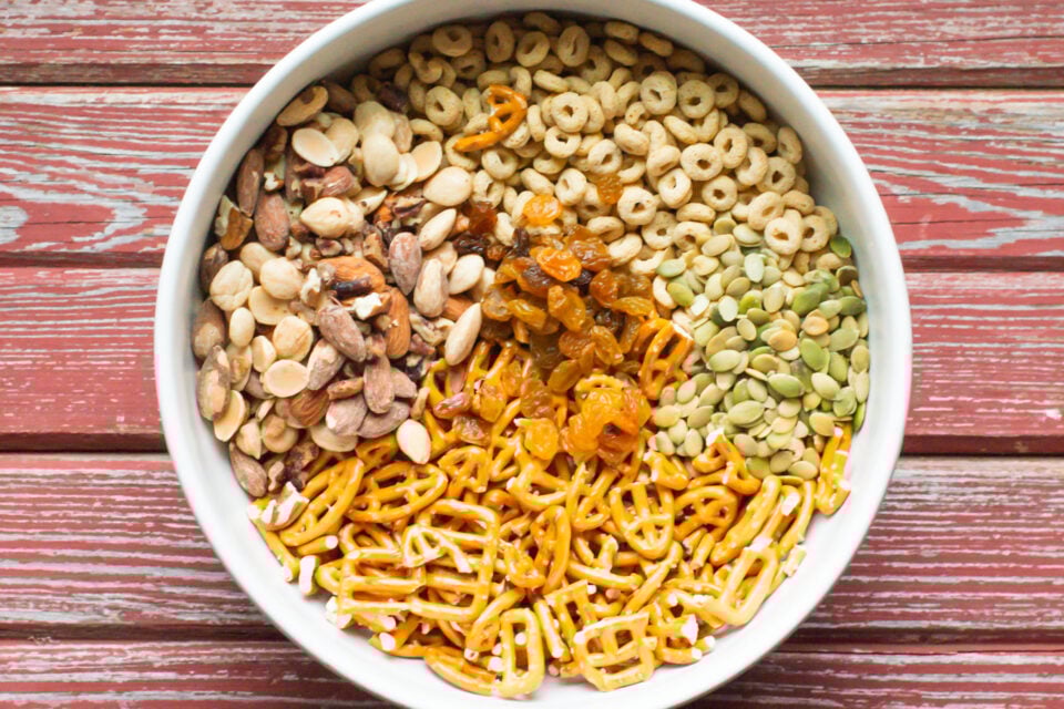 Looking down on a large bowl full of ingredients like cereal, pretzels, nuts, and more.