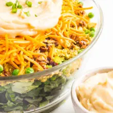 A close-up of Vegan Seven Layer Salad in a large bowl with frozen peas behind it.
