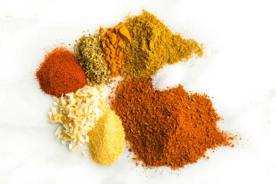 The powders used to make homemade taco seasoning are on a white counter top, including garlic powder, cumin powder, etc.
