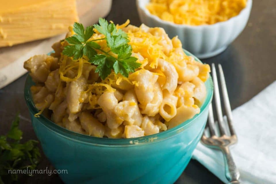 A close-up of a bowl of vegan mac and cheese with a block of vegan cheese and vegan cheddar shreds behind it.