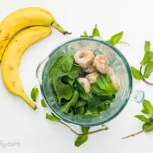 Spinach and bananas are in a blender jar. Next to it are more leaves of spinach and bananas.