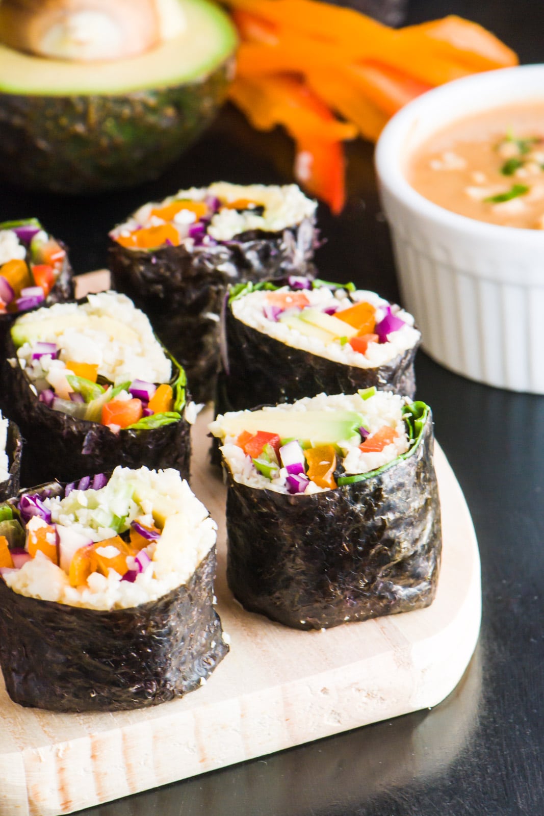 Several slices of vegan sushi sit by a bowl of spicy sweet peanut sauce.