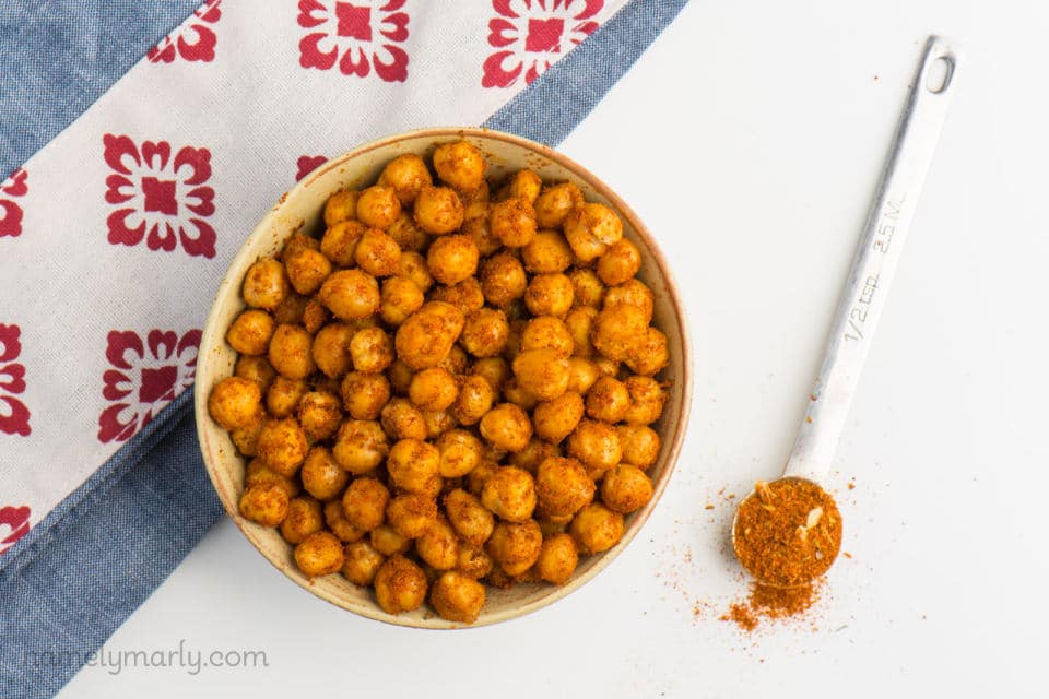 Spicy Roasted Chickpeas are in a bowl with a measuring spoon of spices beside it.