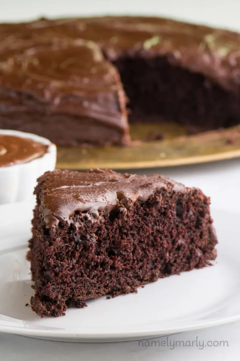 A slice of chocolate cake with chocolate avocado frosting on top sits in front of the rest of the cake.