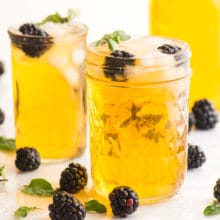 A closeup of two glasses of iced tea infused with blackberries and mint sprigs.