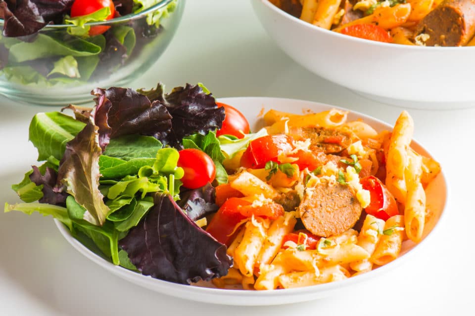 A bowl of easy Vegan Penne Pasta and Sausage with a salad.