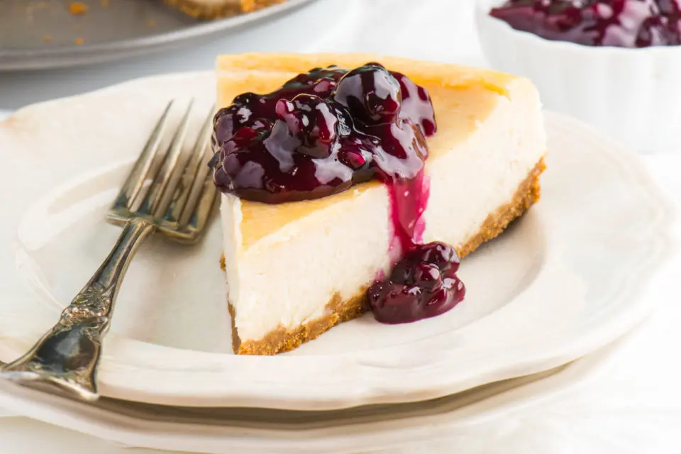 A slice of vegan cheesecake sits on a plate with blueberry sauce on top.