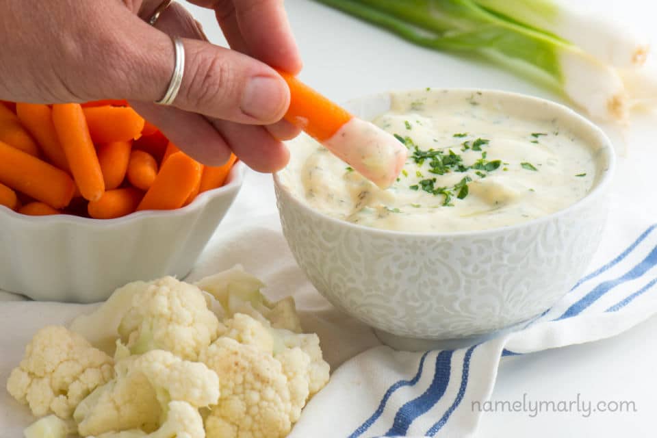 A hand reaches in and dips a carrot in dip.