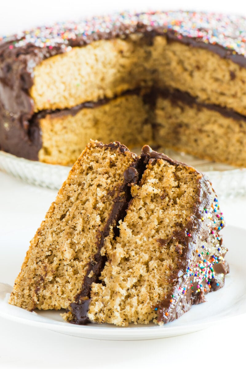 A slice of vegan vanilla wacky cake sits on a plate. The rest of the cake is behind it.