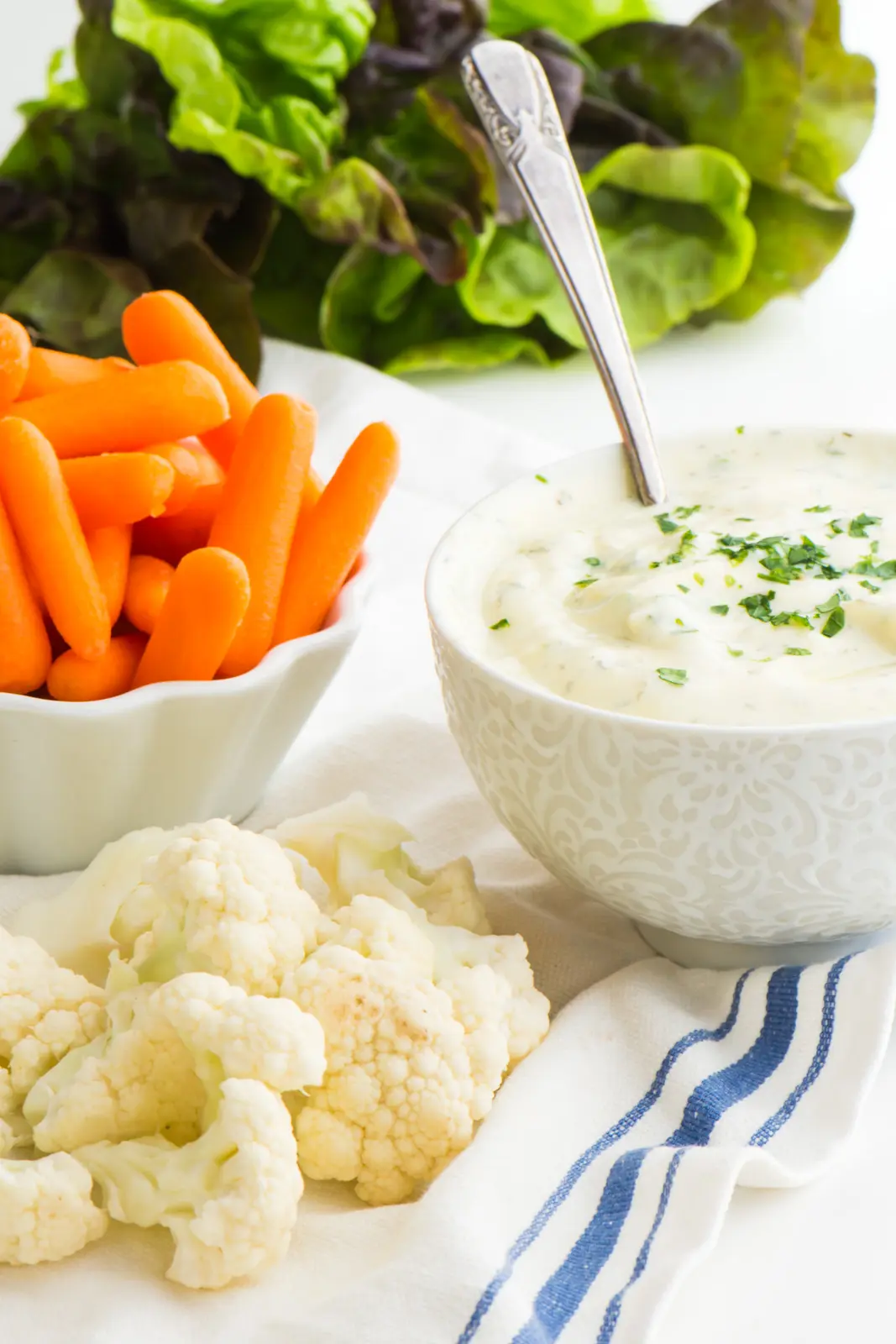 A bowl of dip sits next to baby carrots and cauliflower florets.