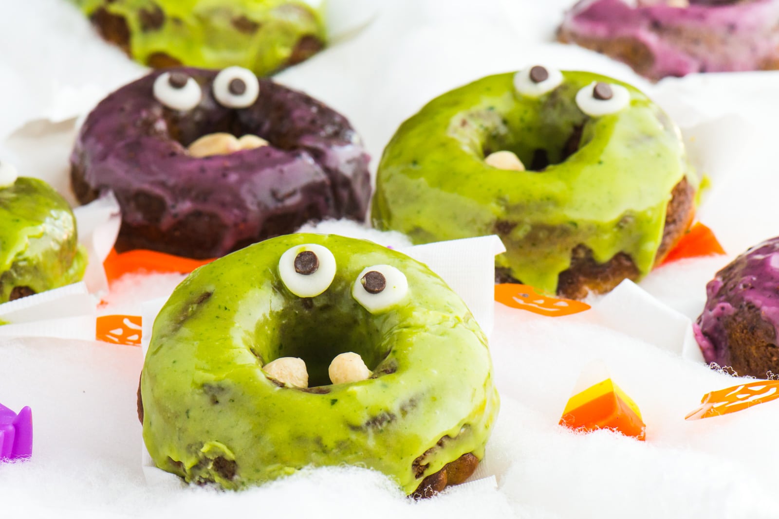 A green halloween donut with a purple and green donut behind it.