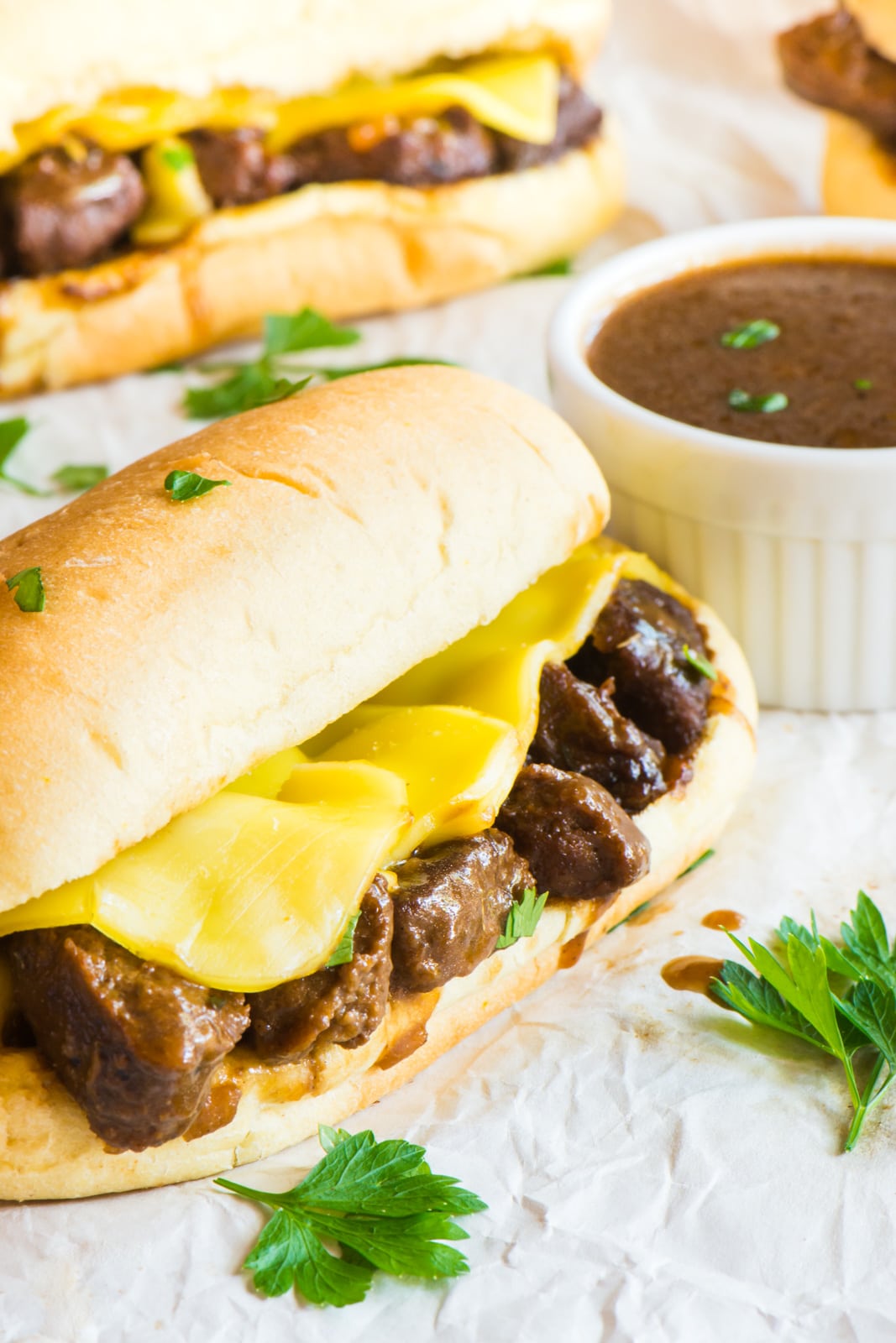 A Vegan French Dip Sandwich with melted cheese. A bowl of sauce and another sandwich is in back.
