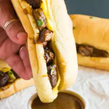 A hand is dipiping a Vegan French Dip Sandwich into a small bowl of sauce.