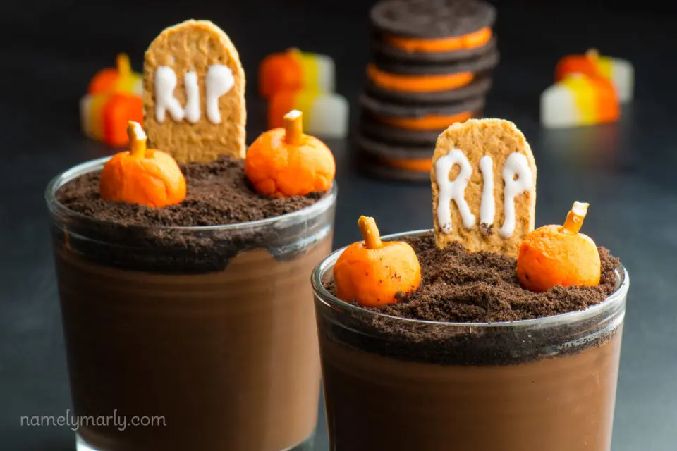 A close-up of pudding cups with candy pumpkins on top and a graham cracker "RIP" tombstone.